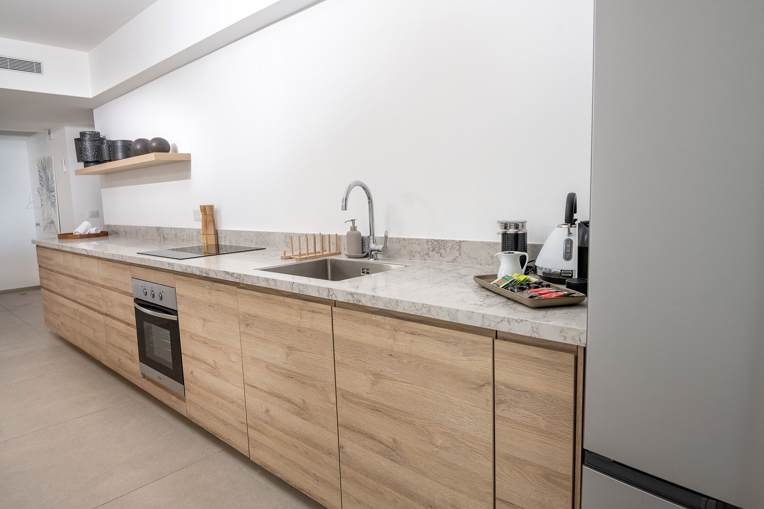A modern kitchen with wooden cabinets, a built-in oven, a double sink, and a coffee machine.