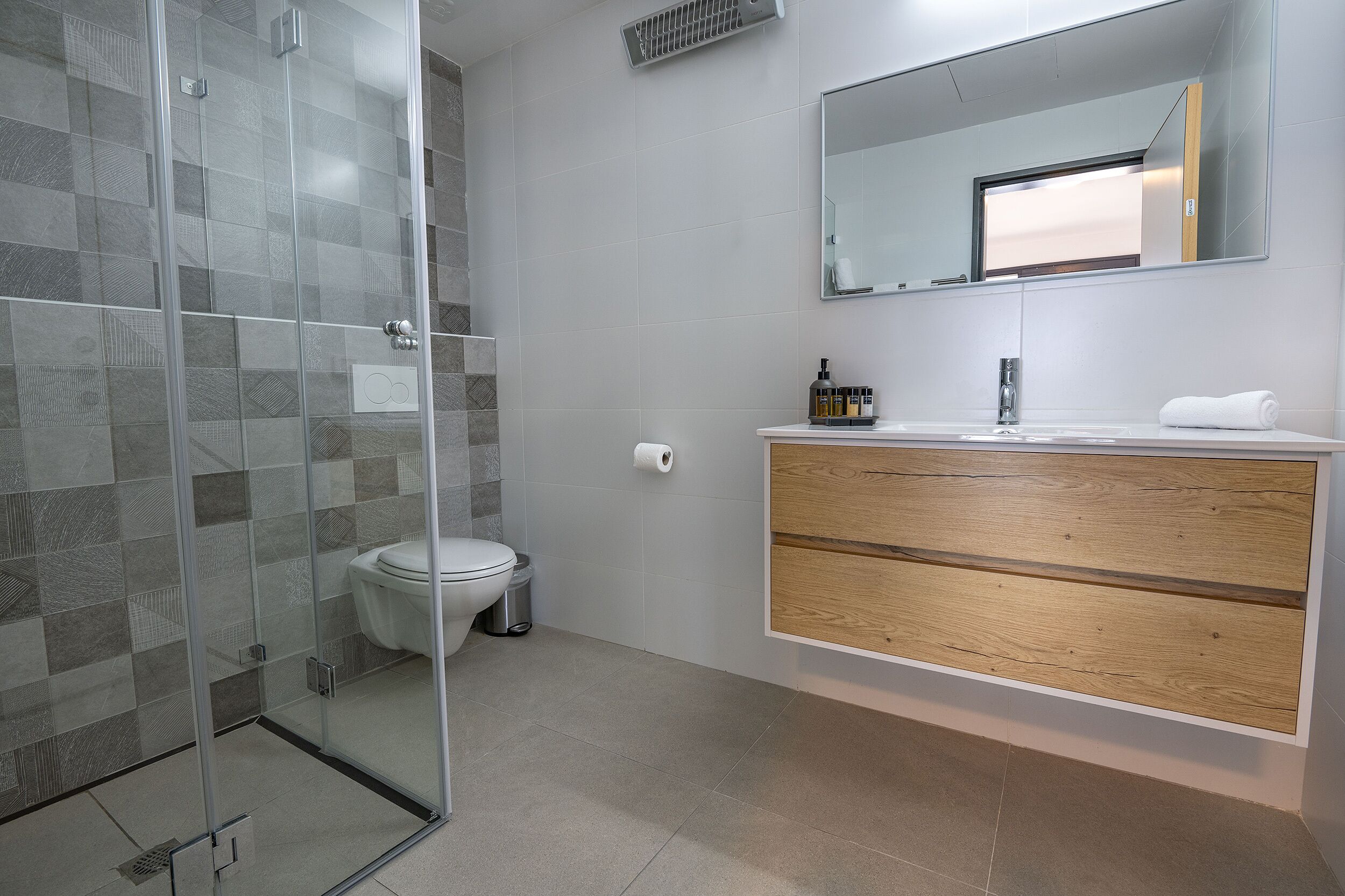 A modern bathroom with a glass shower enclosure, a toilet, and a vanity with a mirror and storage.