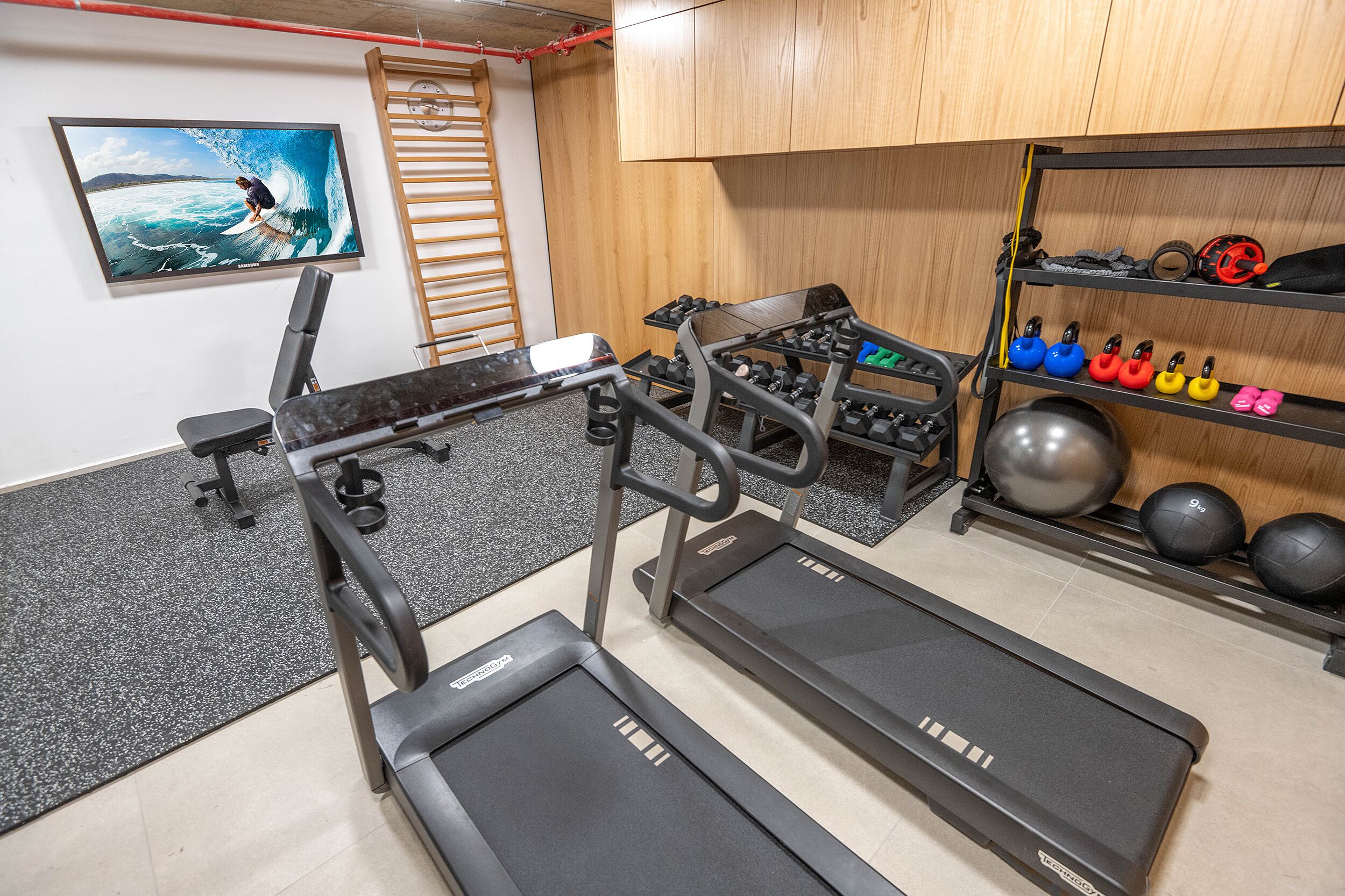 Un gimnasio con cintas de correr, máquinas de pesas y una variedad de mancuernas y pelotas de ejercicio.