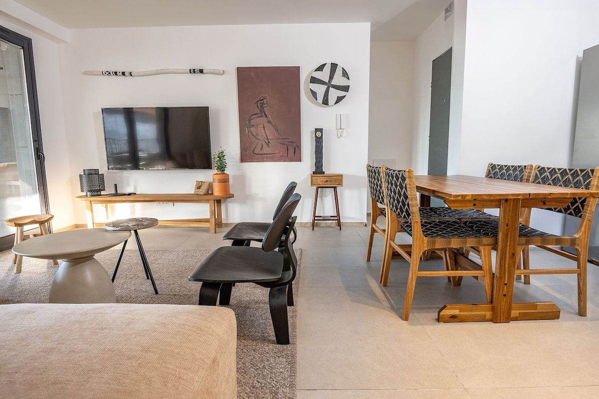Una sala moderna con un televisor de pantalla plana grande, una mesa de comedor de madera y asientos cómodos.