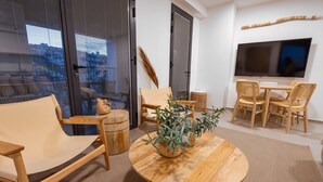 Una sala de estar moderna con una mesa redonda de madera, sillas color beige, un sofá y un televisor montado en la pared.