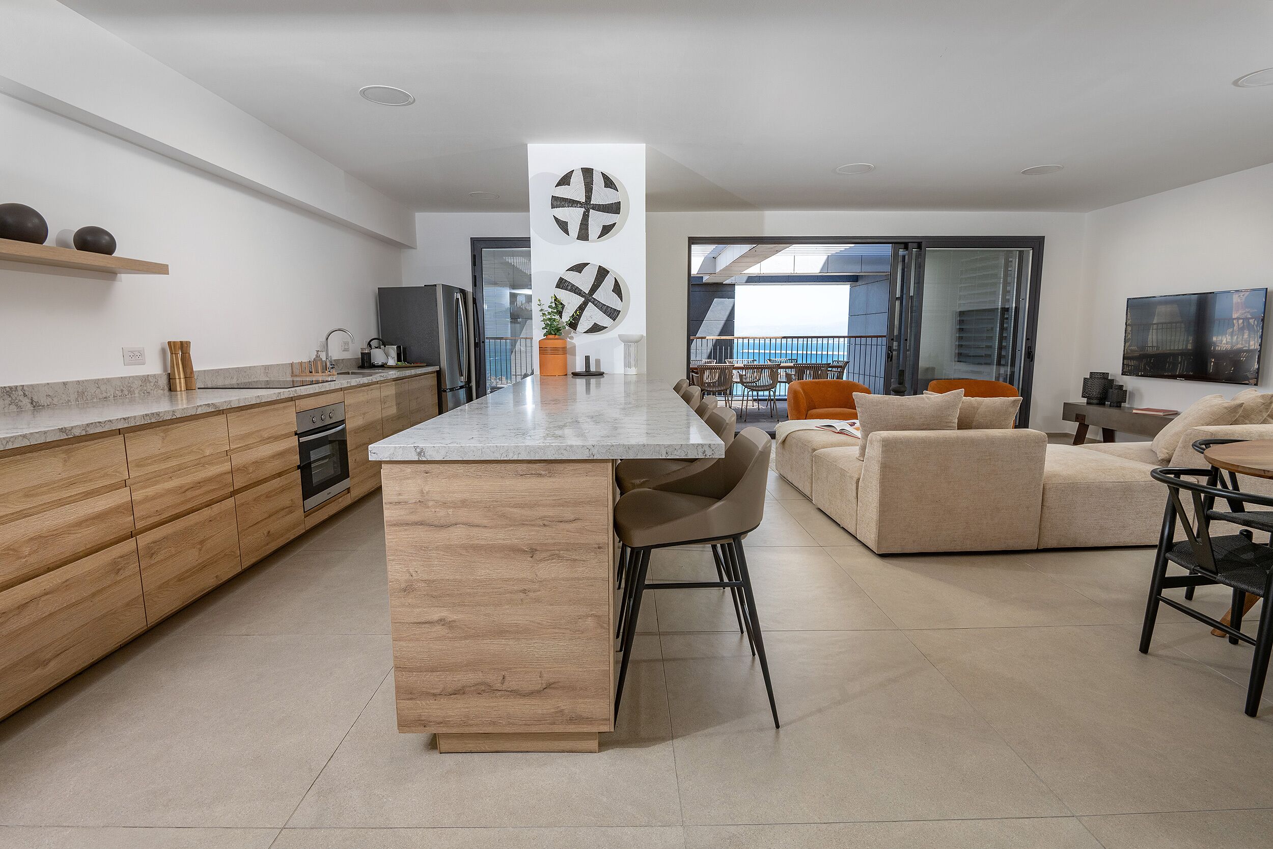 Uma cozinha moderna com uma ilha central, armários de madeira e uma área de refeições com sofá e cadeiras.