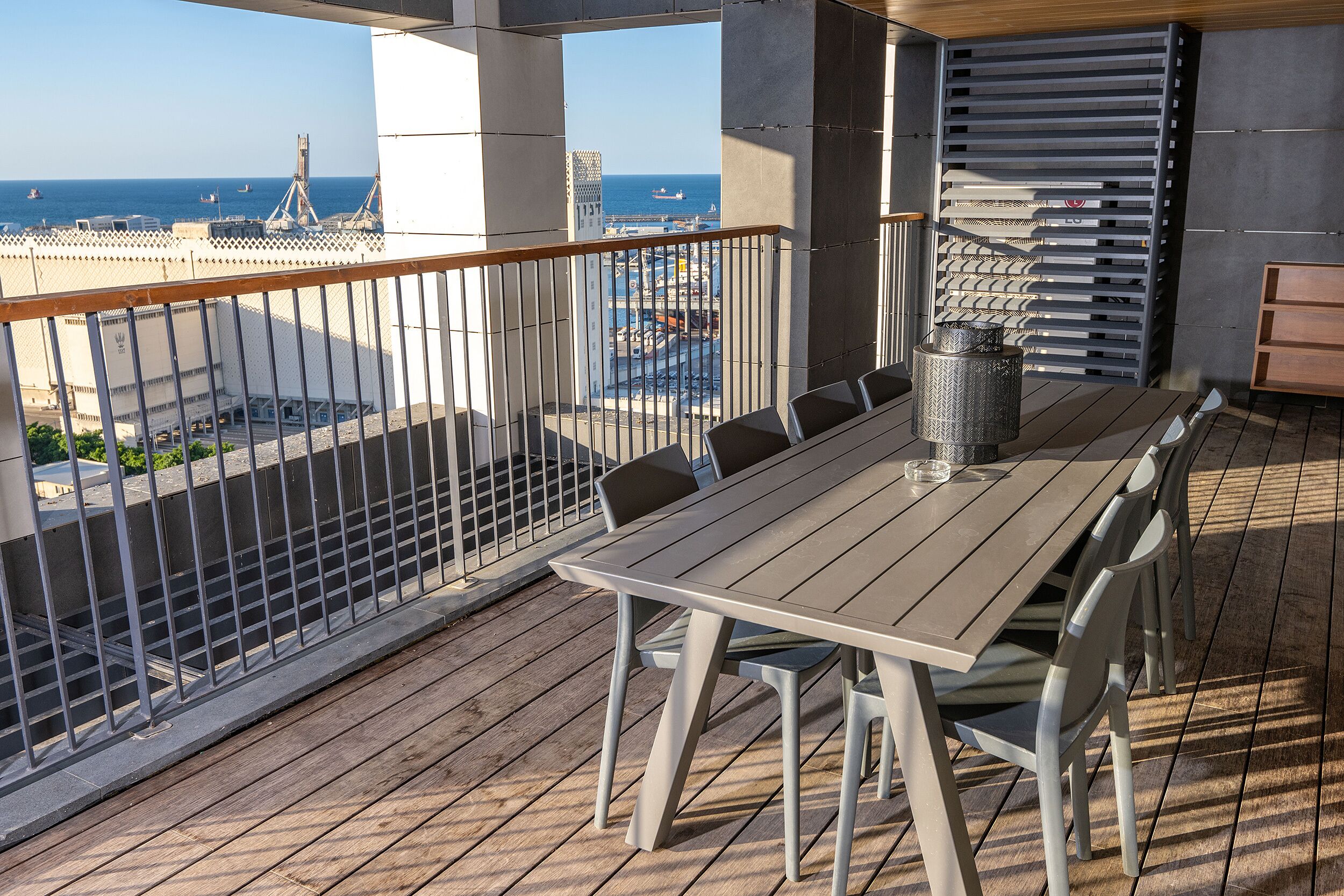 Un balcón con vista al mar, una mesa con sillas y una barandilla de metal.
