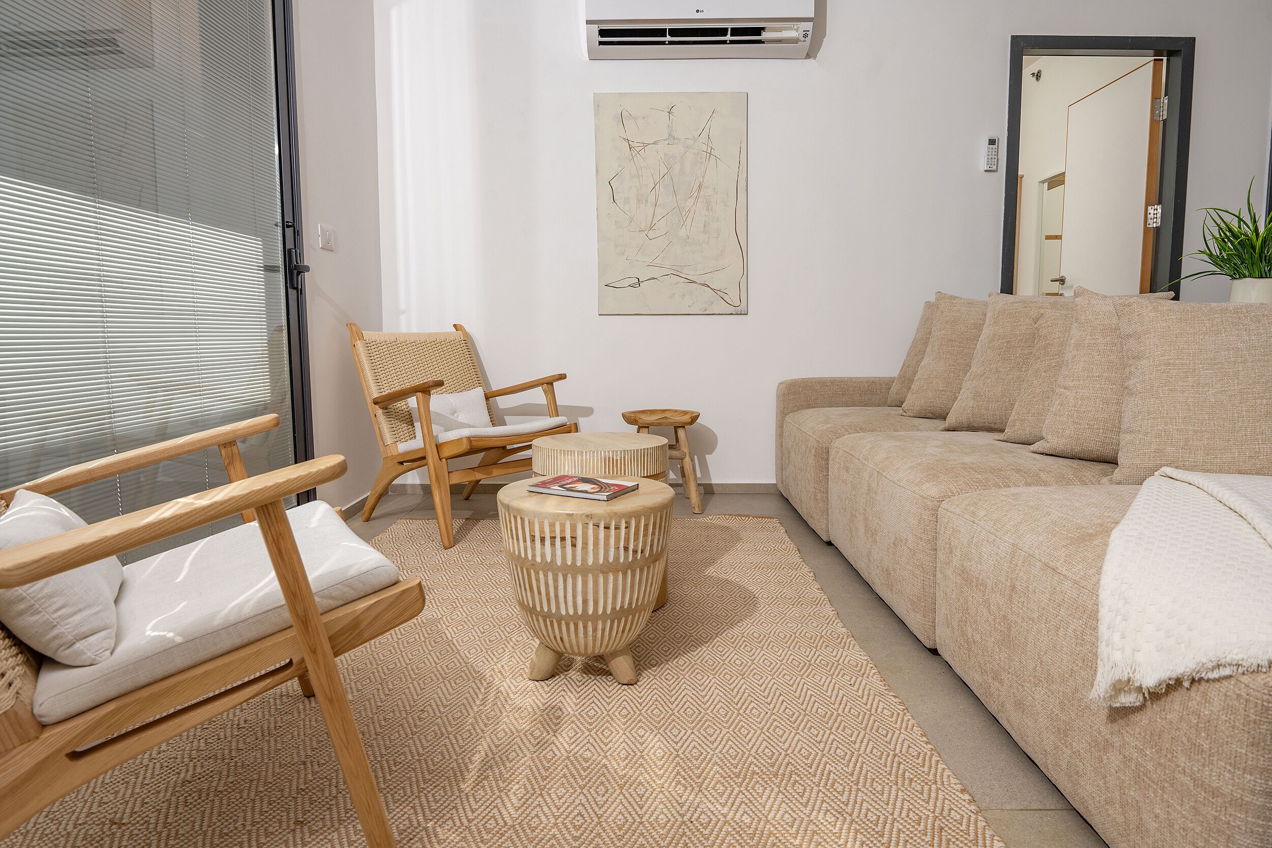 A living room with a sofa, a wooden chair, a small round table, and a large window with blinds.