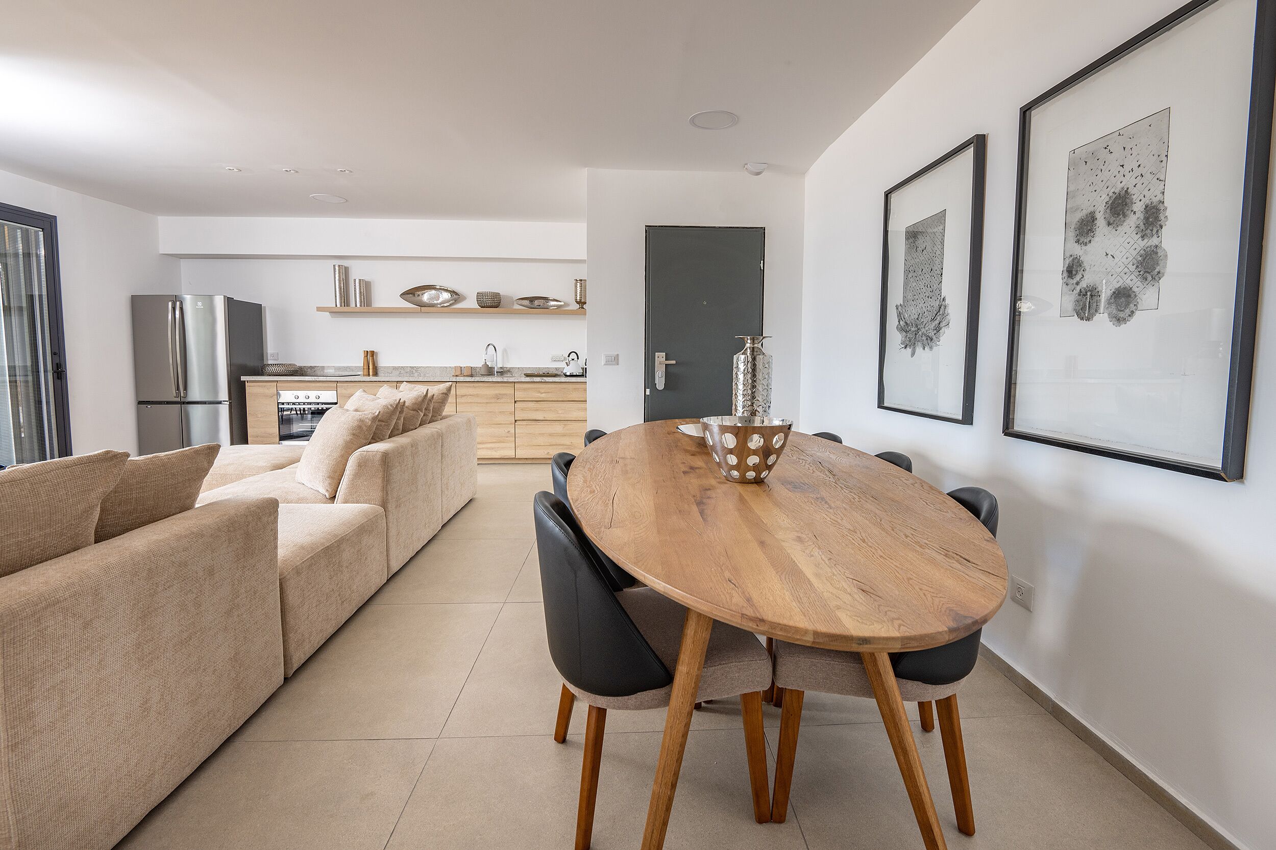 A modern kitchen with a built-in oven and refrigerator, a dining area with a wooden table and chairs, and a living room with a sofa and a coffee table.