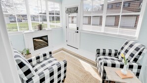 A cozy room with a fireplace, checkered chairs, and large windows overlooking a residential area. - Adorable Little Yellow House, Prime Location! Downtown Pella, IA (Pella)