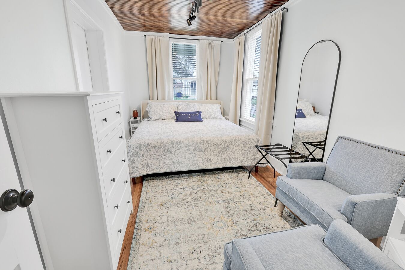 A bedroom with a bed, a grey sofa, a floor lamp, and a large mirror.