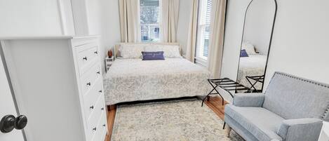 A bedroom with a bed, a grey sofa, a floor lamp, and a large mirror.