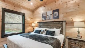 Une chambre aux murs lambrissés, avec un grand lit, une table de chevet et une fenêtre équipée de stores.