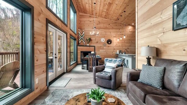 L’intérieur chaleureux d’un chalet avec des murs en bois, une cheminée, un coin repas et un espace salon comprenant un canapé et des fauteuils.