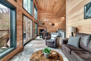 Interior acogedor de una cabaña con paredes de madera, chimenea, comedor y zona de estar con sofá y sillones.