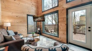 L’intérieur chaleureux d’un chalet, avec un revêtement mural en bois, un canapé, une table basse et une grande fenêtre donnant sur une terrasse.