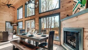L’intérieur d’une maison en rondins moderne, avec un coin repas, de grandes fenêtres et une cheminée.