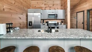 Une cuisine dotée de plans de travail en granit, d’appareils électroménagers en acier inoxydable et de panneaux muraux en bois.