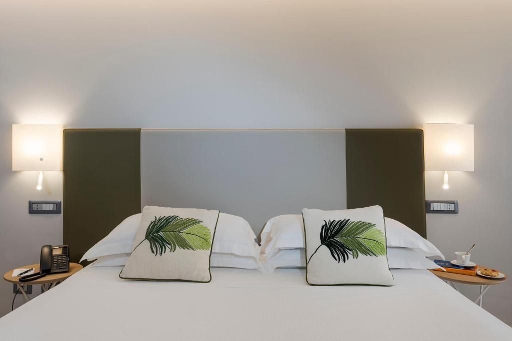 Ein Hotelzimmer mit einem Bett, zwei Nachttischlampen, einem Nachttisch mit Telefon und einem kleinen Tisch mit Teller und Tasse.