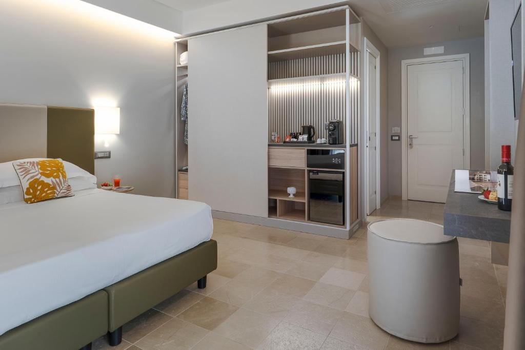 A modern hotel room with a bed, a wardrobe, a small kitchenette, and a bathroom.