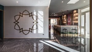 Un vestíbulo moderno con un mural geométrico, una recepción y una zona de bar.