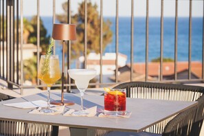 A table with three drinks, a lamp, and a view of the sea. - Hotel Netum Mare (Noto)