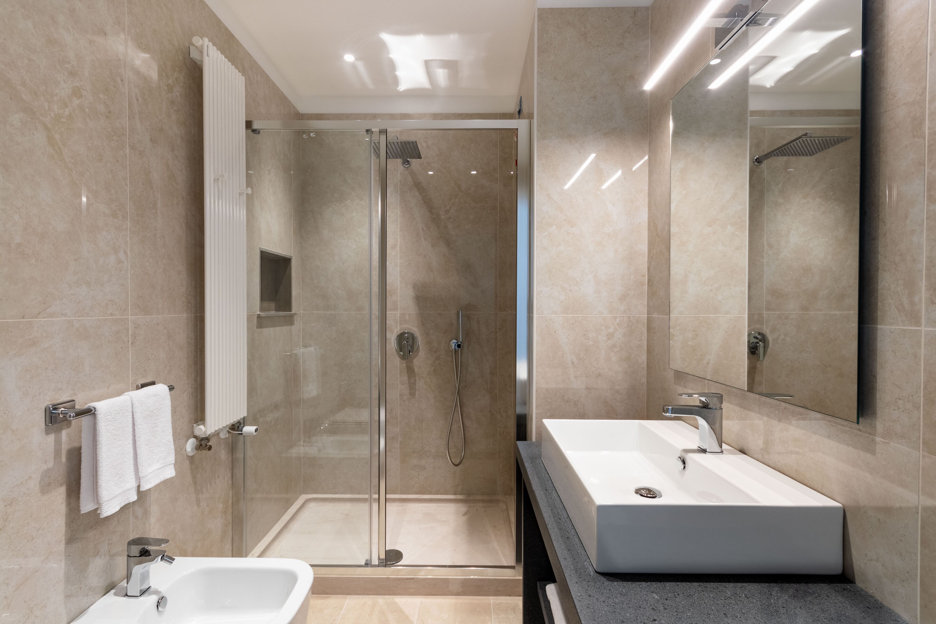 A modern bathroom with a glass-enclosed shower, two sinks, and a large mirror.