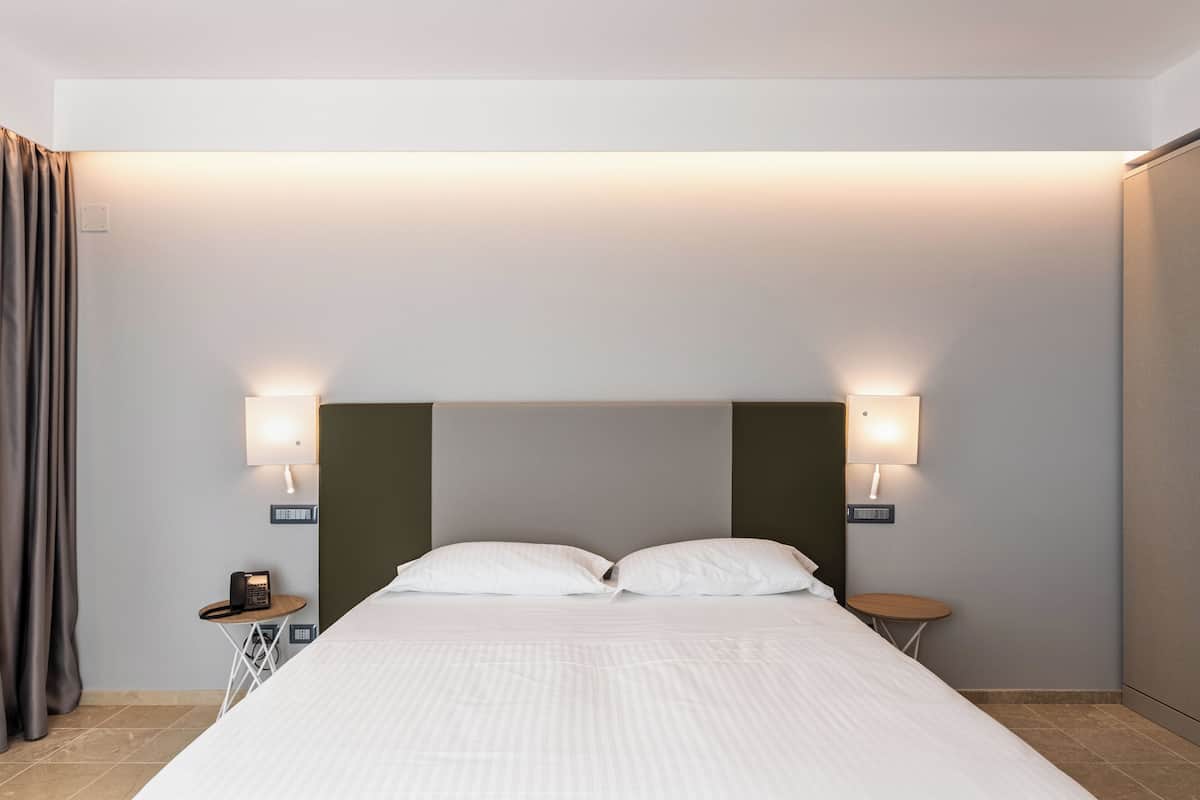 Una habitación de hotel con una cama, dos lámparas de noche, una mesita con un teléfono y una cortina.