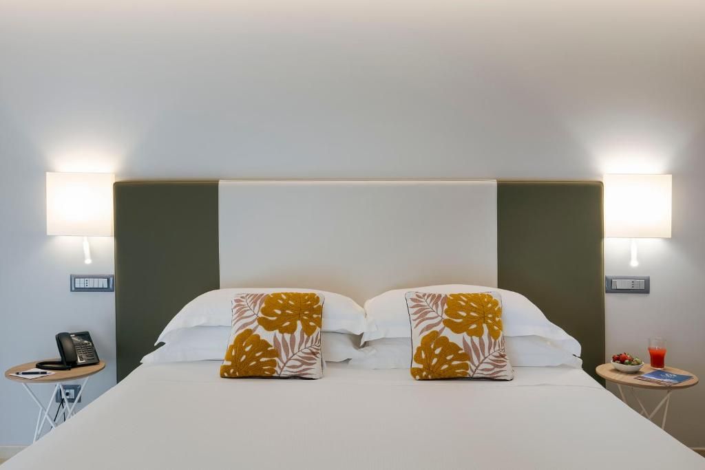 Une chambre d’hôtel avec un lit, deux lampes de chevet, une petite table avec un téléphone et une table d’appoint sur laquelle se trouvent un verre de jus de fruits et un bol de fruits.
