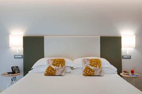 A hotel room with a bed, two bedside lamps, a small table with a phone, and a side table with a glass of juice and a bowl of fruit. - Hotel Netum Mare (Noto)