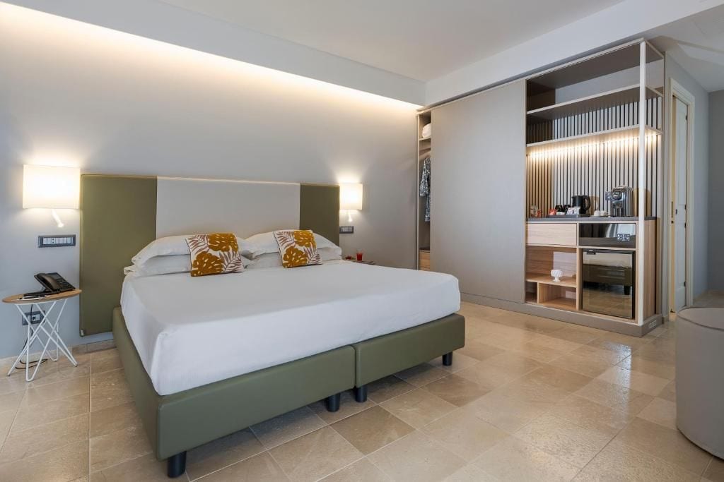 Una habitación de hotel moderna con una cama grande, lámparas de noche, una mesita y un vestidor.