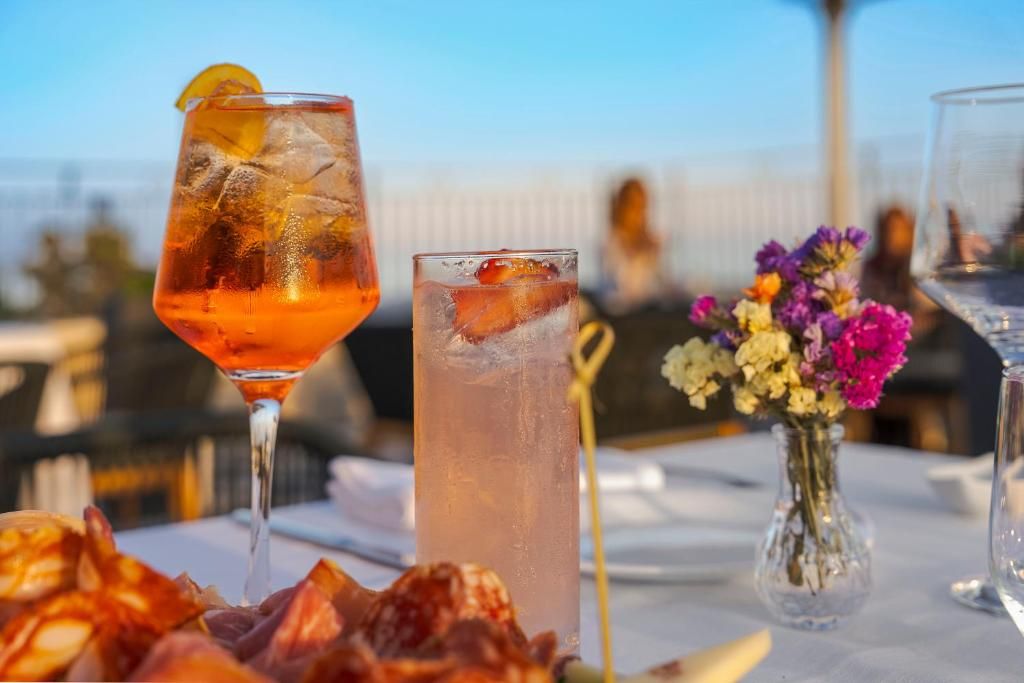 Una mesa con dos vasos de bebidas, un florero con flores y un plato de comida.