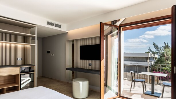 Habitación de hotel moderna con cama, escritorio, televisor y balcón con sillas.