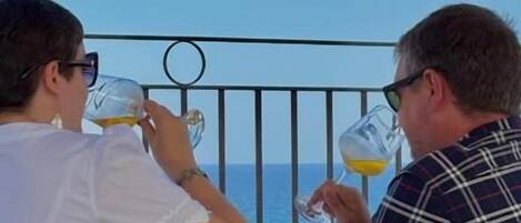 Two people seated at a table with a view of the sea, a metal railing, and a tablecloth.