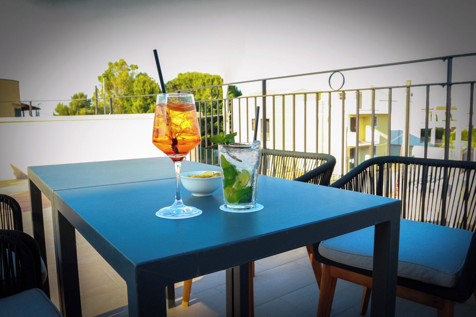 Een tafel met twee drankjes en een schaal met snacks op een balkon.