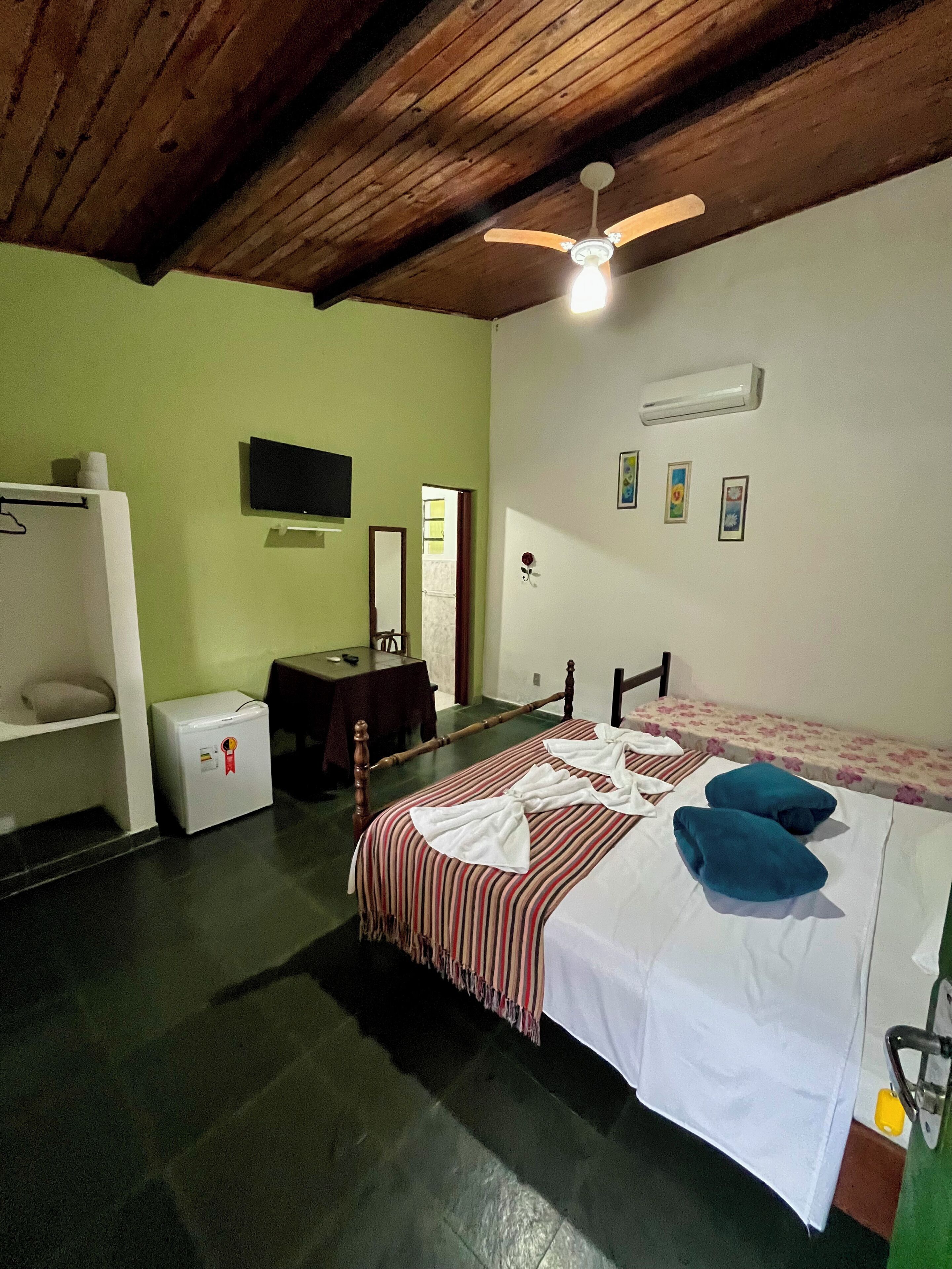 Une chambre à coucher comprenant un lit, une télévision, une petite table, une armoire et un ventilateur de plafond.