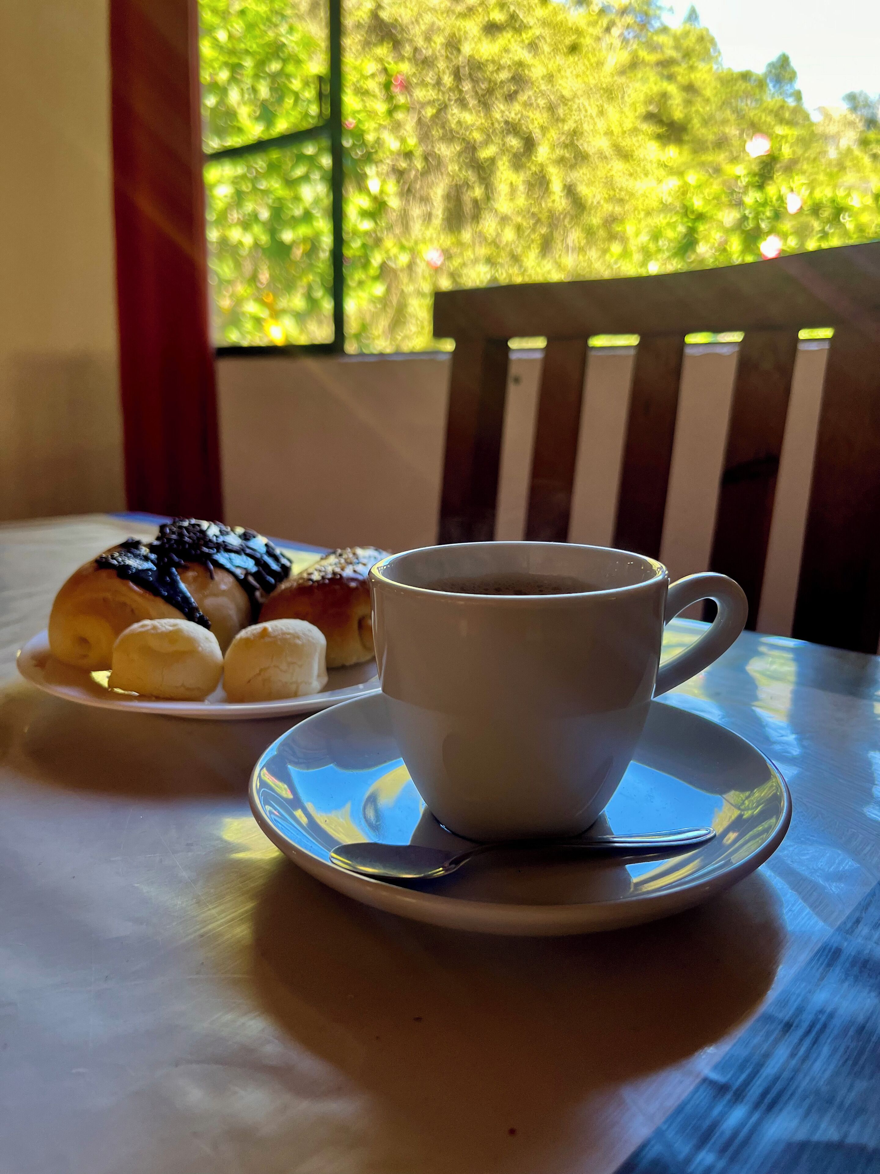 Una taza de café sobre un plato con pasteles en el fondo.