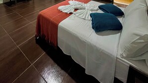 Een slaapkamer met een bed, een bureau, een stoel, een televisie en een raam met gordijnen.