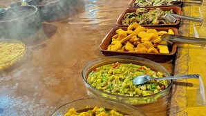 Een buffet met diverse gerechten, waaronder een kom gele curry, een schotel met groene groenten, en verschillende vleesschaaltjes.