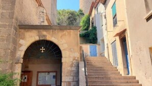 Une rue étroite avec un escalier en pierre menant à un bâtiment surmonté d’une horloge et dont on aperçoit, au fond, un clocher.
