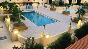Une piscine entourée de plantes en pot et de palmiers, avec un bâtiment en arrière-plan.