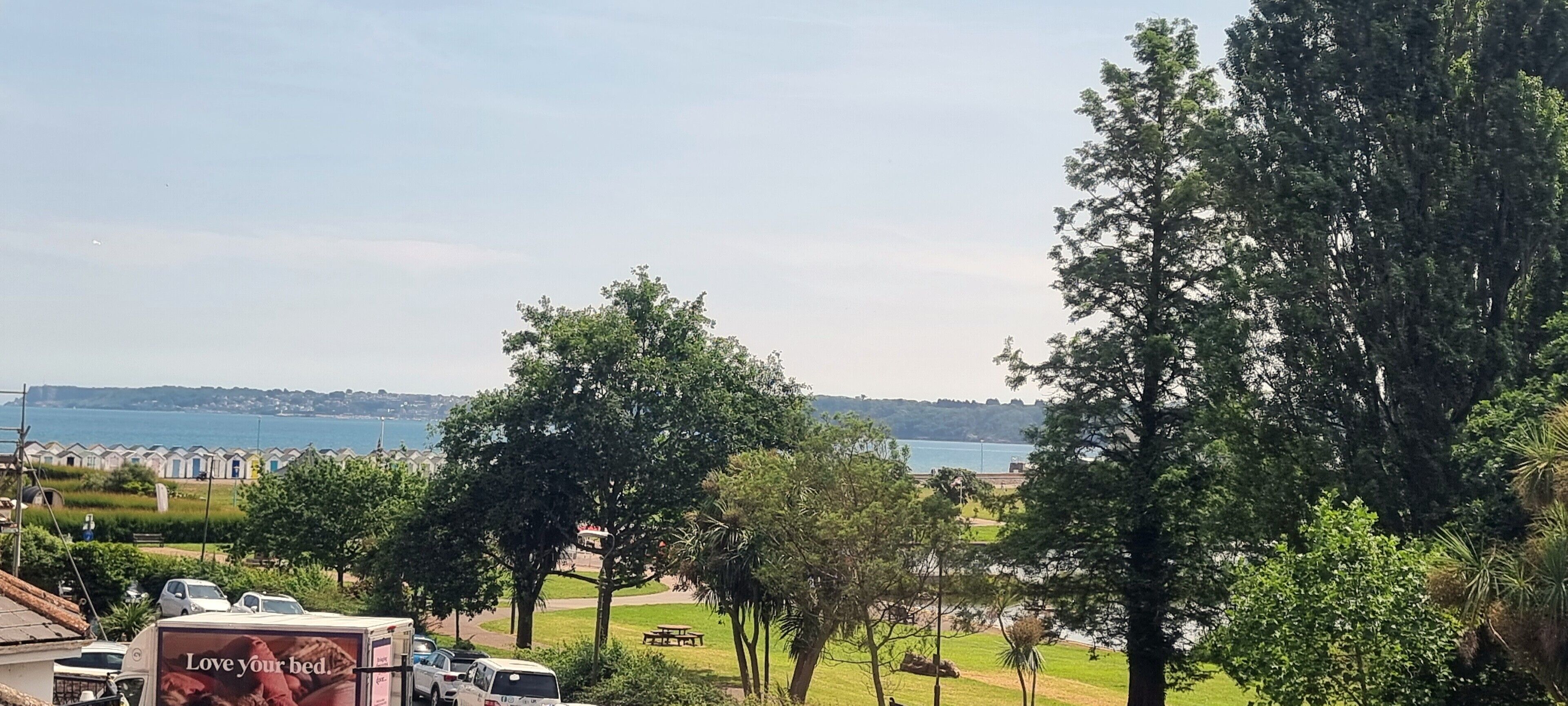 Egy tengerparti táj látképe, amelyen látható egy strand, fák és a távolban egy városképlet.