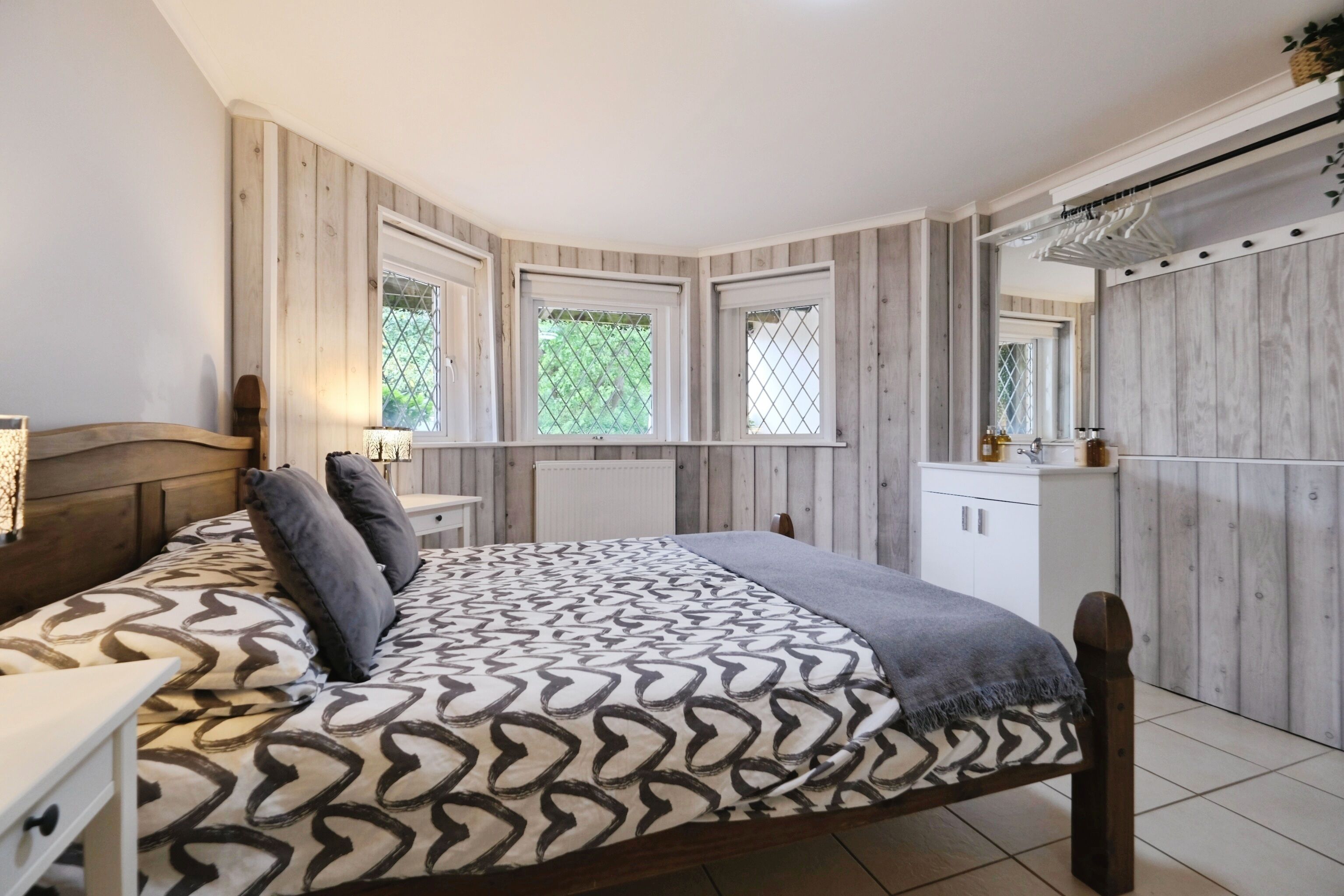 A bedroom with a bed, bedside table, dresser, and a window with a view of greenery.