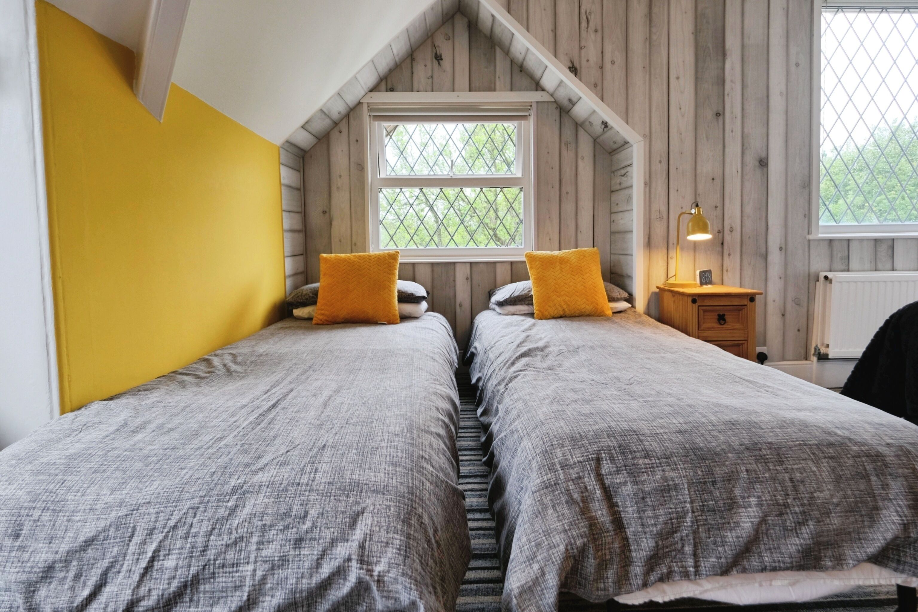 A bedroom with two beds, a window, and a nightstand with a lamp.