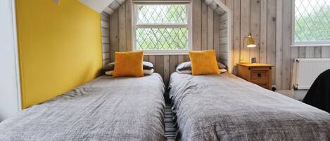 A bedroom with two beds, a window, and a nightstand with a lamp.