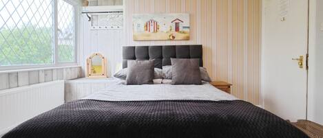 A bedroom with a large bed, a headboard, a painting on the wall, and a window with a view of greenery.