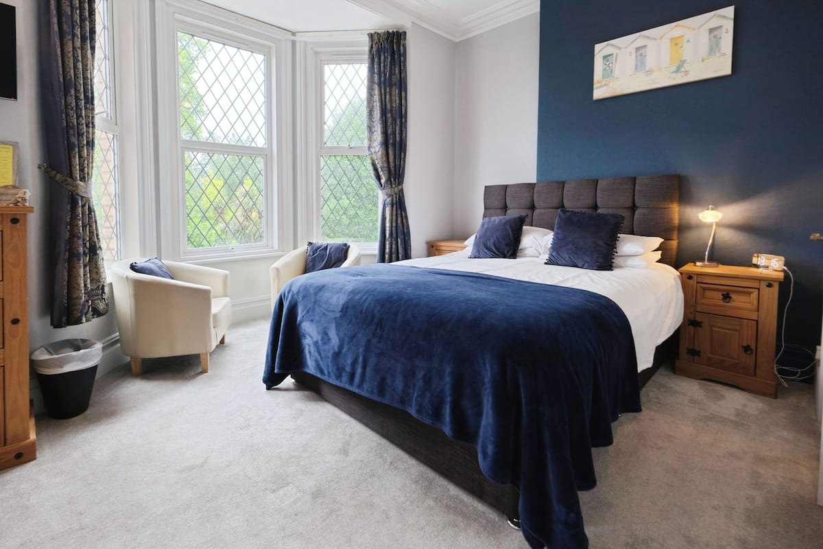 A bedroom with a large bed, a nightstand, a chair, and a window with curtains.