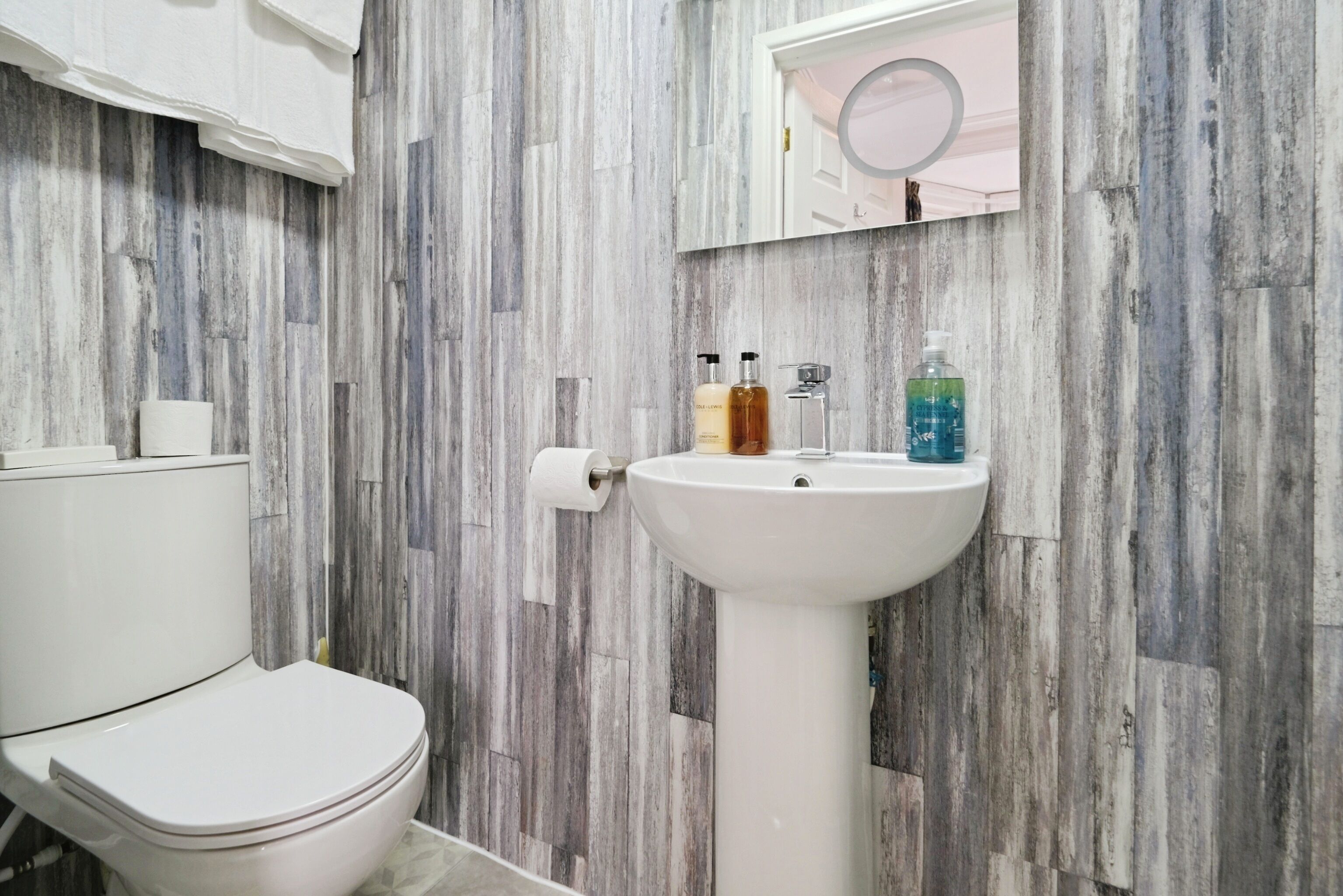 Ein Badezimmer mit Toilette und Waschbecken in Weiß sowie einem Spiegel über dem Waschbecken.