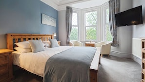 A bedroom with a large bed, a television, a chair, and a window with curtains. - Rowcroft Lodge  (Paignton)