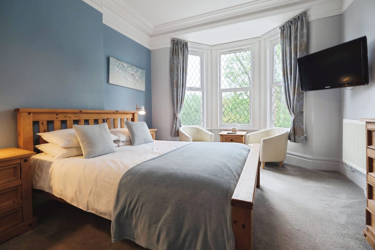 A bedroom with a large bed, a television, a chair, and a window with curtains.