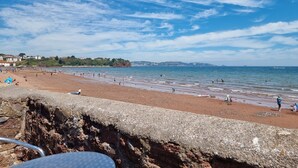 A beach with a rocky foreground and a view of the sea and distant buildings. - Rowcroft Lodge  (Paignton)