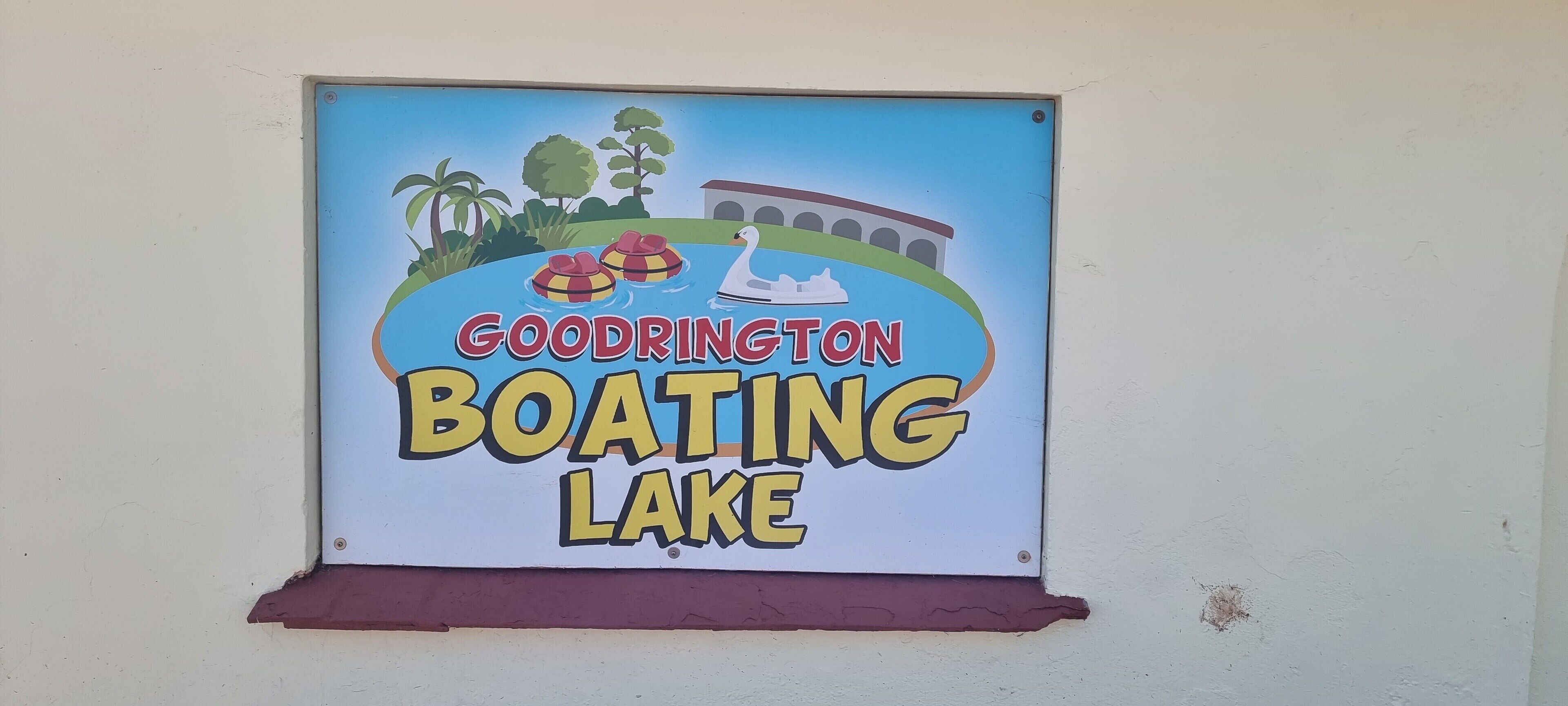 A sign for Goodrington Boating Lake with a swan, paddle boats, and a bridge.