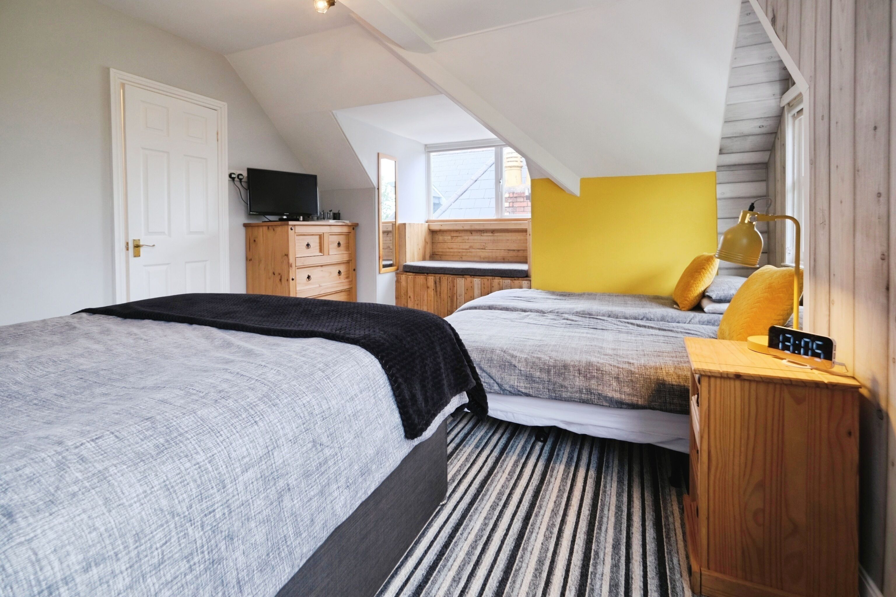 A bedroom with two beds, a wooden dresser, a television, and a window with a view of the outside.