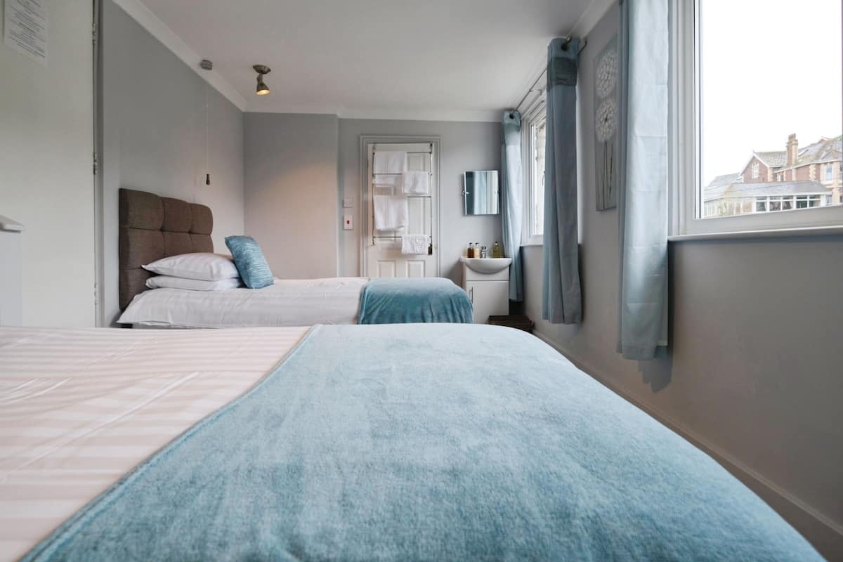 A hotel room with two beds, a bathroom with a sink and mirror, and a view of buildings through the window.